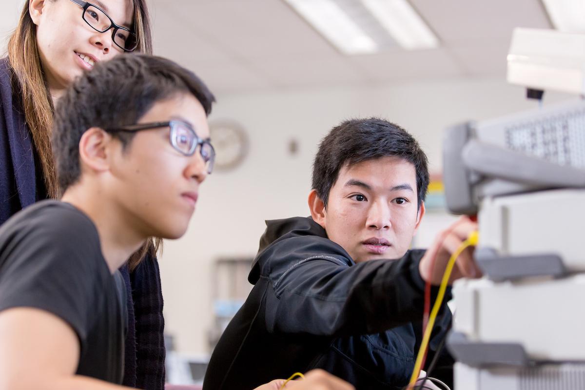 A student talks to his two peers as he points to a stack of electronic devices.